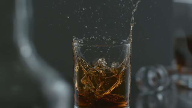 Ice is dropped into glass of whisky in slow motion