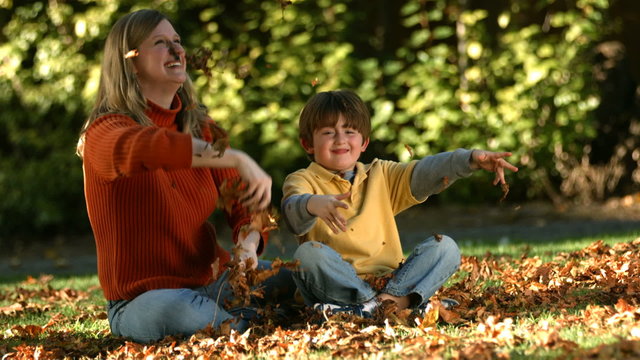 mom and son playing in autumn leaves together 
