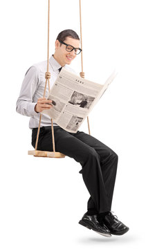 Young man reading newspaper seated on a swing