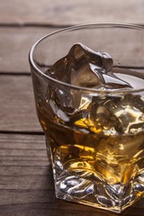 Glass of whiskey and ice cubes on wooden surface