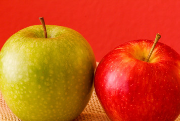 Manzanas / Una manzana verde y otra roja, llenando el encuadre sobre manten de arpillera. Fondo rojo.