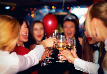 group of happy elegant women clinking glasses in limousine, hen party