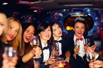 group of happy elegant women clinking glasses in limousine, hen party