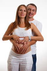 Pregnant Woman and Her Husband holding  hands in a heart shape on her belly.