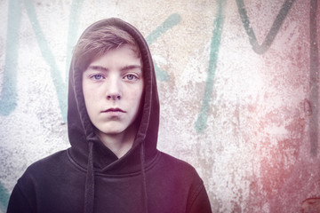 portrait of a teenage boy with black hoodie in front of a graffi