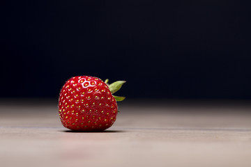 single strawberry on a table with black background