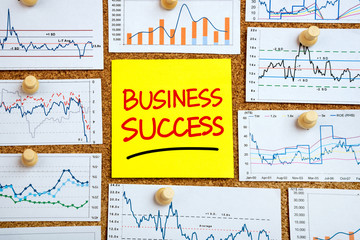 business success handwritten on post-it with financial graphs