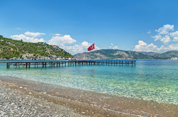 view of clear sea, mountains and pier from pebble beach