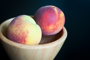 Fresh peaches served in a simple wooden fruit bowl isolated on a black background.