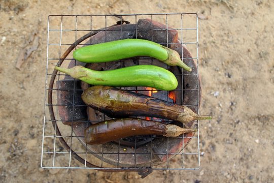 Grilling eggplants on earthen stove, old style Asian cooking. Half done, half raw