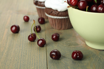 Chocolate cupcakes with cherries with a bowl of cherries on a wooden background