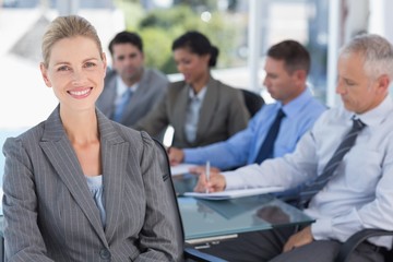 Businesswoman smiling at camera with colleagues behind