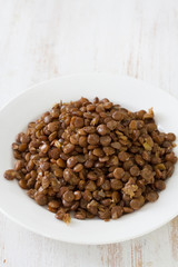 boiled brown lentil on plate on white wooden background
