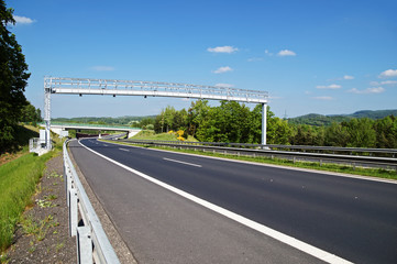 Electronic toll gate above an empty highway in a wooded landscape