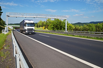 White truck passing through the electronic toll gates on the highway in a wooded landscape