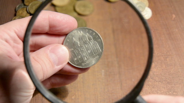 numismatist considers old coins through magnifying glass