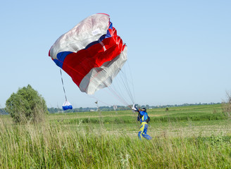 Colorful red white parachute on clear blue sky skidiver landing on the green field