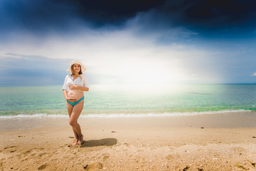 Fototapeta premium pregnant woman posing on beach and looking at the sun over the s