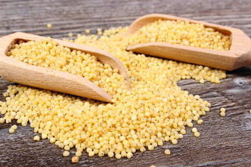 Heap of millet groats with spoon on wooden background