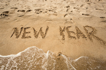 New Year written on sand and being washed by waves