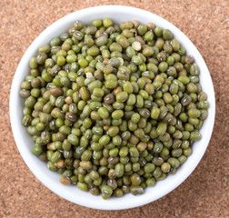 Mung beans in white bowl on cork board background