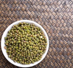 Mung beans in white bowl on wicker background