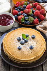 crepes, fresh berries and jams on wooden table, vertical