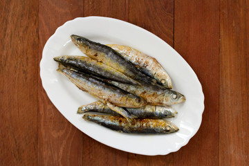 fried sardines on white dish on brown wooden background
