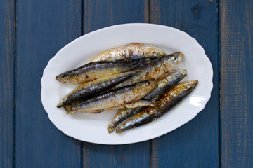 fried sardines on white dish on blue wooden background