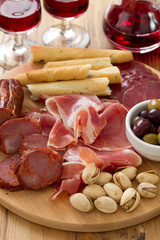 meat appetizer with olives and nuts on tray on brown wooden background