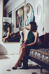 Fashion photo of gorgeous woman with dark hair in elegant green silk dress posing in luxurious interior