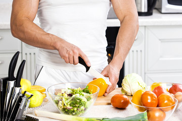 Handsome man cooking at home preparing salad in kitchen.