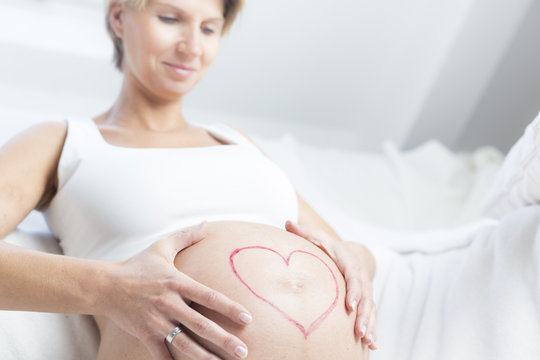 Schwangere Frau hält Babybauch mit Herz