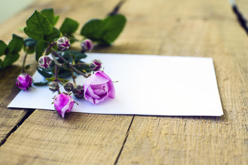 sheet of paper and roses on wooden background