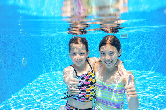 Happy children swim in pool underwater, girls swimming, playing and having fun