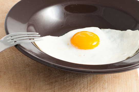 view of a fried egg served on dark dish with fork