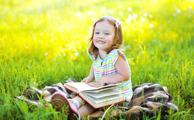 Portrait of little smiling girl child with book sitting on the g