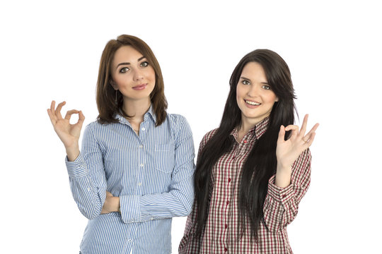 Two cheerful girls makes OK hand sign.
Beautiful smiling women casual dress checkered shirts brunette on white background