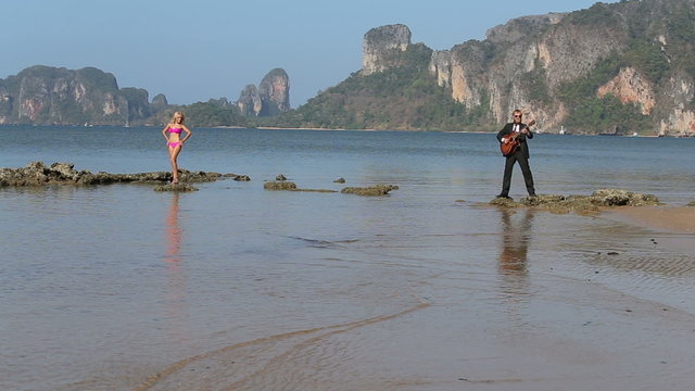 guitarist plays girl in swimsuit looks at low tide	