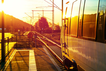 Modern passenger train standing at countryside platform with beautiful landscape at sunset.