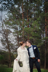 Happy bride and groom walking on the edge of a pine forest in the spring