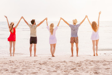 Summer beach at sunset. A group of five people holding hands and raises his arms to the sky. There are two young men and two young women during a day of rest in the sea with deserted beach