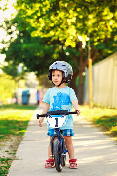 Portrait of a little boy toddler riding a bicycle in helmet on the road outside outdoors on a bright sunny spring summer day, seasonal child activity concept, healthy lifestyle