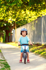 Portrait of a little boy toddler riding a bicycle in helmet on the road outside outdoors on a bright sunny spring summer day, seasonal child activity concept, healthy lifestyle