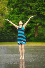 Portrait of happy young white Caucasian  girl jumping in puddles during the rain thunderstorm on a bright summer day outside, sports recreation leisure activity and freedom, freeze motion effect