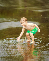 Portrait of happy toddler boy playing with water in puddles during the rain thunderstorm on a summer day outside, recreation leisure concept, childhood freedom, motion blur and freeze motion effect