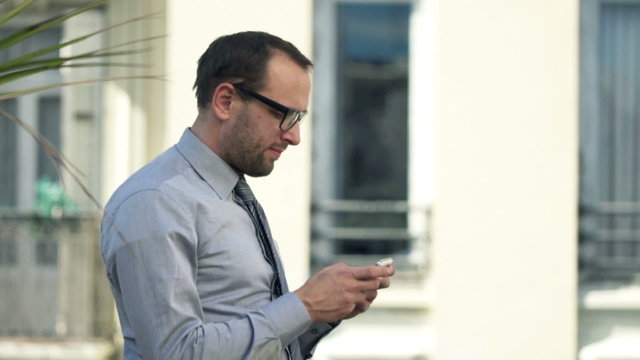 Young businessman using smartphone standing on balcony 
