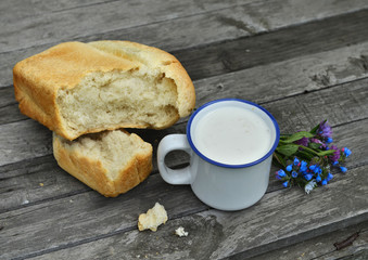 Close up of milk in mug and loaf of bread with flowers 