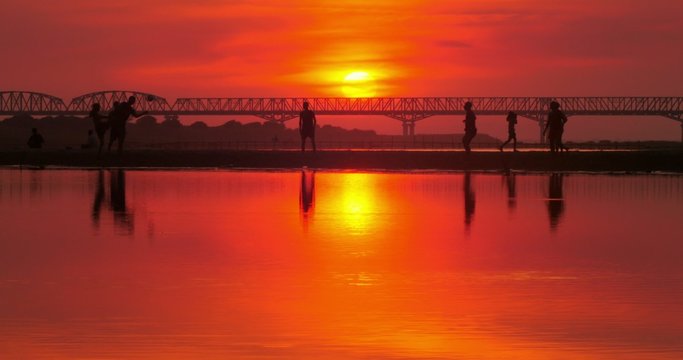 People play soccer on river shore. Silhouettes of players reflect in calm water