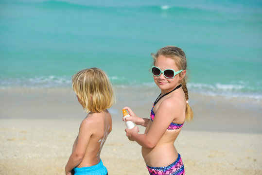 Side view sister applying sunscreen cream on brother's back at beach